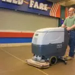 Operator pushing Advance Adfinity walk-behind scrubber to clean business floors.