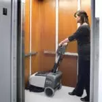 Advance SC351 walk-behind scrubber and operator cleaning elevator floor.