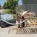 Operator vacuuming up outdoor empty pallet area with Advance SW8000 rider sweeper hose.