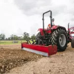Mahindra 6075 utility tractor smoothing out rocks on road.