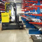 Combilift C6000 ST Stand On Multi-Directional Forklift in narrow aisle warehouse.