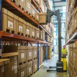 Combilift COMBI-WR Reach Stacker lifting box off shelf in warehouse.