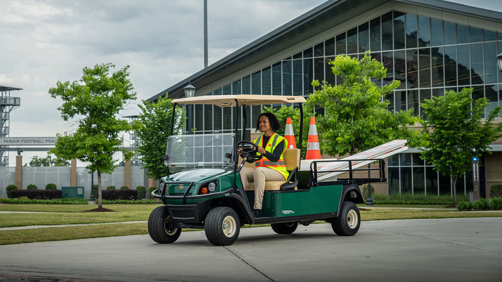 Maintenance worker driving Cushman Shuttle 2 utility vehicle with materials in the bed.