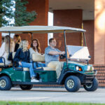 Cushman Shuttle 6 driving outdoors with 5 passengers.