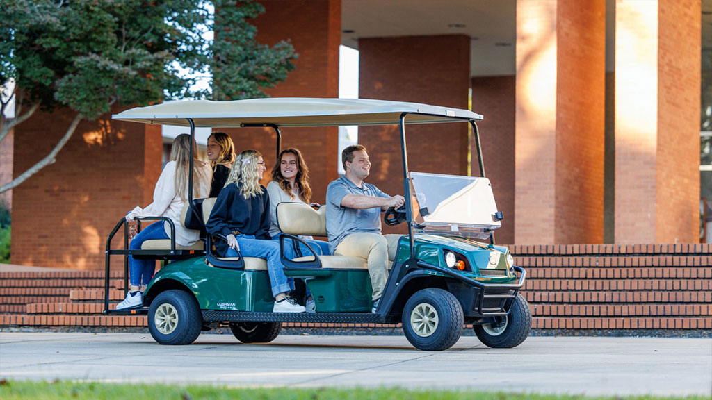 Cushman Shuttle 6 driving outdoors with 5 passengers.