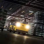 Cushman Titan XD burden carrier driving through dark beverage facility with headlights on.