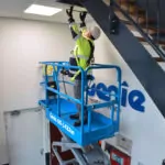 Genie GS-1432m with repairman raised to ceiling in bucket of scissor lift.
