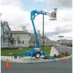 Genie TZ-34/20 trailer-mounted boom lift lifting worker to repair street light.