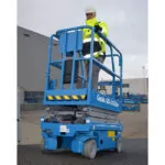 Worker in bucket of Genie GS-1432m scissor lift driving in parking lot.