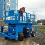 Worker driving across muddy path on jobsite in Genie GS-4390 scissor lift.