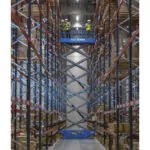 Workers raised Genie GS-4655 scissor lift in warehouse aisle.