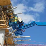 People in bucket of Genie S-80 XC telescopic boom lift at construction site.