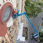 Genie SX-105 XC aerial boom lift raising employees to repair building features.