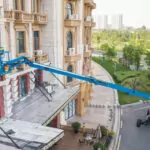 Genie SX-105 XC telescopic boom lift raising employees to work on building.