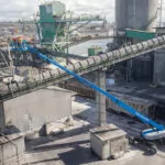 Workers raised in bucket of Genie SX-125 XC boom lift at outdoor site.