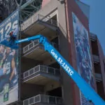 Genie SX-135 XC aerial lift lifting workers next to a football sign.