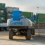 Back of Genie SX-150 telescopic boom lift with employees in the bucket, close to the ground.