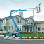 Genie TZ-34/20 trailer-mounted boom lift raising worker to repair residential street light.