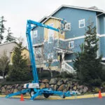 Genie TZ-50 trailer mounted boom lift raising worker to put siding on a house.