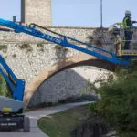 Genie Z-33/18 boom lift raising operator to trim tree branches.