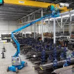 Genie articulating boom lift lifting operator to ceiling in metal work shop.