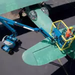 Repairman being raised by Genie Z-45/25J DC boom lift to fix vintage green airplane tail.