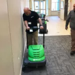 Worker cleaning building hallway carpets with IPC Eagle SmartVac 464 walk-behind vacuum sweeper.