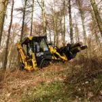 JCB 1CXT Backhoe Loader driving up a hill carrying logs.