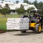 JCB 504-13 Telehandler carrying materials on a pallet on sand road.