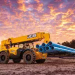 JCB 510-56 Telehandler carrying pipe materials on work site.