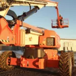 JLG 1250AJP articulating boom lift driving on path at outdoor facility.