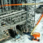 JLG Ultra Boom Lift raising worker over large metal rack structure.
