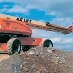 JLG 1350SJP Ultra Series boom lift driving across dirt and rock terrain.