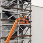 Workers raised in JLG 1350SJP boom lift at building construction site.