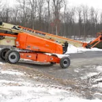 JLG 1500AJP articulating boom lift driving down rocky, snowy hill.