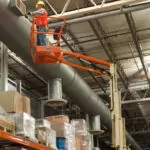 JLG 26E toucan mast boom lift extended to warehouse ceiling.