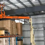 Worker raised to warehouse ceiling in JLG 32E boom lift platform.