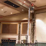 JLG 38AM push around Vertical Mast Lift raising worker to the ceiling of a large room.