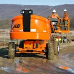 JLG 460SJ aerial boom lift driving on muddy terrain.