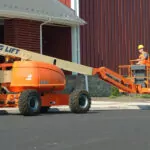 Farmer driving JLG 600AJ articulating boom lift on a paved path.