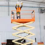 Worker lifted on JLG ES2646 electric scissor lift inside large garage.