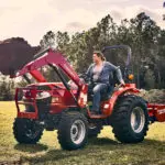 Mahindra 1626 Compact Utility Tractor: bucket raised lifting dirt while driving on grass.