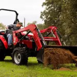 Mahindra 2638 compact utility tractor transporting dirt in grass field.