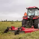 Mahindra 2670 compact utility tractor with cab mowing field of grass.