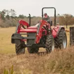 Mahindra 6065 utility tractor driving in grass field.