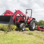 Mahindra 6075 utility tractor with bucket attachment driving in grass field.