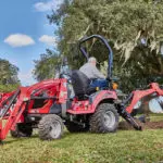 Mahindra eMax20S HST sub-compact tractor digging in grass with backhoe attachment.
