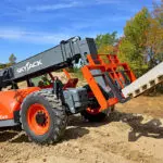 Skyjack SJ843 TH Telehandler driving on dirt transporting pallet of materials on construction site.