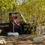Pro XD Mid-Size Gas Utility Vehicle by Polaris Commercial driving up dirt hill on work site.