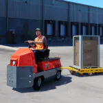 Taylor-Dunn Huskey C-426 AC tow tractor hauling trailer near warehouse.